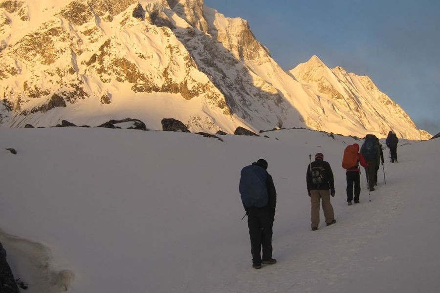 Line of trekkers walking across snowy glacier with golden mountain peaks at sunrise